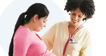 A Female doctor listens with a stethoscope on a pregnant woman's belly